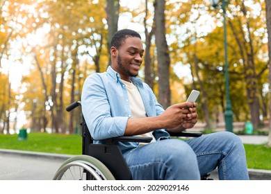 Cheery disabled black guy in wheelchair using mobile phone, checking email or messages at autumn park. Young handicapped Afro guy with cellphone posting in social network, browsing web outside - Powered by Shutterstock