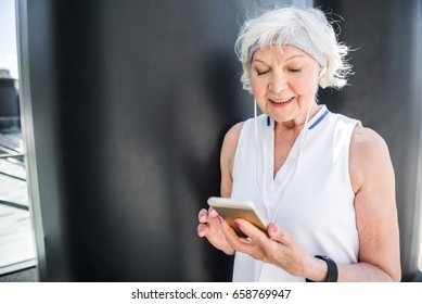 Cheery elderly lady texting through mobile phone outdoor