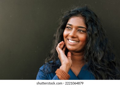 Cheery Indian Woman Looking Aside While Standing Over Dark Background Outdoors