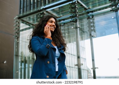 Cheery indian woman talking on mobile phone while walking through city street - Shutterstock ID 2232198791