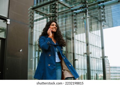 Cheery indian woman talking on mobile phone while walking through city street - Shutterstock ID 2232198815