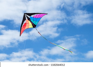Cheery multi-colored tailed kite flying against blue sky with spotted clouds.