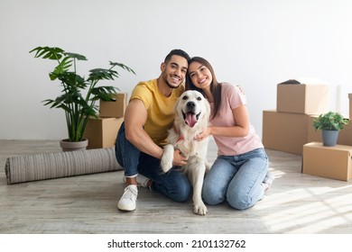 Cheery young international couple with cute golden retriever dog sitting on floor of new home on relocation day. Happy millennial husband and wife with cute pet moving to new house - Shutterstock ID 2101132762