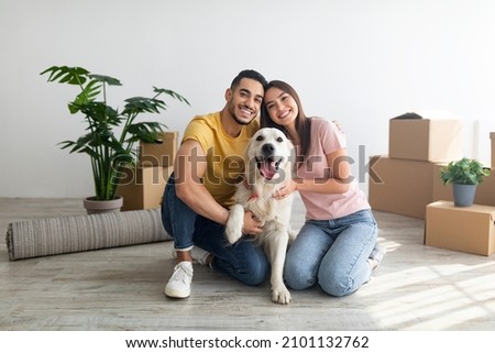 Cheery young international couple with cute golden retriever dog sitting on floor of new home on relocation day. Happy millennial husband and wife with cute pet moving to new house