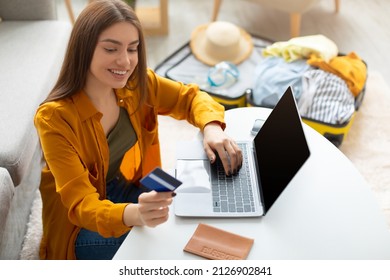 Cheery Young Lady Using Credit Card And Laptop Pc With Mockup For Online Travel Agency Website, Booking Abroad Trip, Making Hotel Reservation On Web From Home, Free Space