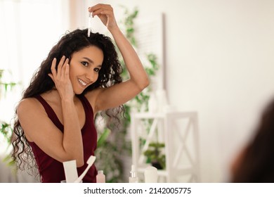 Cheery young woman applying serum on damaged dry hair near mirror at bathroom, empty space. Natural cosmetics for haircare, split ends treatment, beauty routine concept - Shutterstock ID 2142005775
