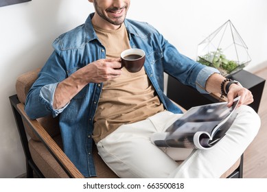Cheery youthful guy resting with mug of hot beverage indoor