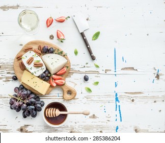 Cheese appetizer selection or wine snack set. Variety of cheese, grapes, pecan nuts, strawberry and honey on round wooden board over rustic white backdrop, top view, copy space - Powered by Shutterstock