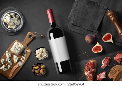 Cheese appetizer selection or wine snack set. Red wine, variety of cheese, figs, bread, olives and prosciutto on wooden board over black backdrop, top view, copy space