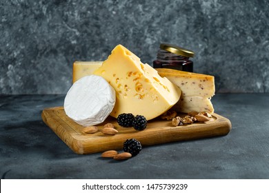 Cheese Assortment on a dark stone background with copy space. Different types: Camembert, cheese with spices, Dutch cheese on wooden cutting board. almond, blackberries and jam with cheese. Soft focus - Powered by Shutterstock