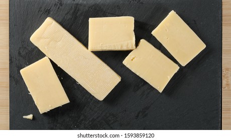 Cheese Block Slices And Black Surface On Wooden Chopping Board, Top View