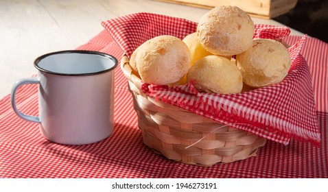 Cheese bread, basket lined with red and white fabric filled with cheese bread on a checkered towel and a white cup, selective focus.