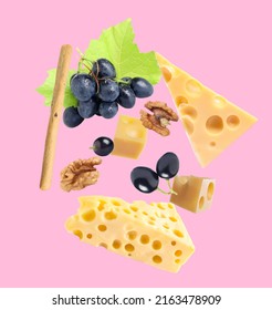 Cheese, Breadstick, Grapes And Walnut Falling Against Pale Pink Background