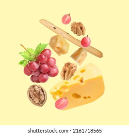 Cheese, Breadstick, Grapes And Walnuts Falling Against Pale Light Yellow Background