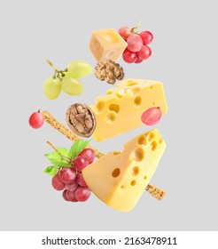 Cheese, Breadstick, Grapes And Walnuts Falling Against Light Grey Background