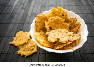 Cheese Chips Snack in a round white bowl on a black wooden background. Grain Free Dippable Crispy Cheddar Cheese Chips, Keto & Low Carb. Crunchy chip from cheddar, parmesan, asiago, herbs, spices
