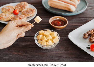 Cheese cube is picked up with a toothpick from glass bowl, surrounded by snacks like pizzas and hotdogs at bar or diner - Powered by Shutterstock