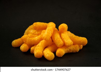 Cheese curls. Crunchy corn puffs, a bunch tasty cheese snacks on a black background. 