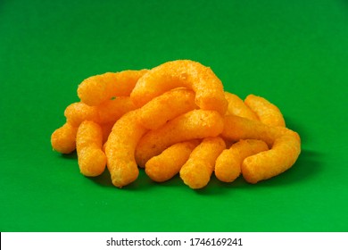 Cheese curls. Crunchy corn puffs, a bunch tasty cheese snacks on a green background. 