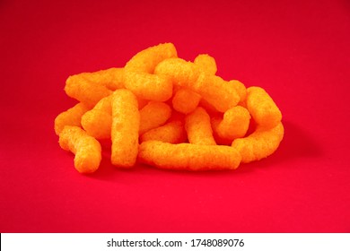 Cheese curls. Crunchy corn puffs, a bunch tasty cheese snacks on a red background. 