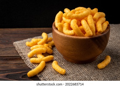 Cheese flavored puffed corn snacks on wooden background. - Shutterstock ID 2022683714