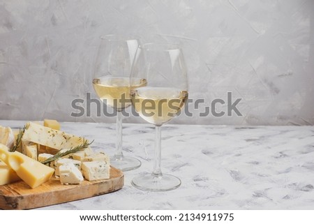 Cheese and a glass of white wine on a grey background. Different cheeses on a wooden board. Cheese set. Empty tablecloth for product montage. Free space for your text