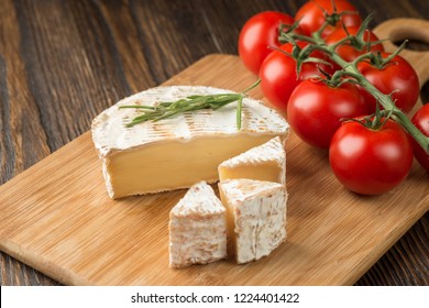 Cheese head of Brie cheese and rosemary and cherry tomato on wood cutting board, rustic style.