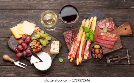 Cheese, meat, grapes and olives antipasto. Appetizer selection on wooden board and glasses with red and white wine. Top view. Flat lay