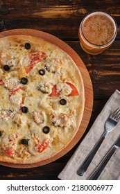 Cheese Pizza With Tomatoes And Olives On A Wooden Plate And A Glass Of Light Beer On The Table In The Pub Top View. Vertical Orientation, No People