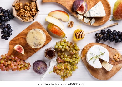 Cheese plate with blue cheese, brie, truffle hard cheese with grapes, figs, pears, honey, fruits and nuts on white table. Top view.  - Powered by Shutterstock