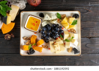 Cheese Plate With Grapes, Honey, Prunes And Walnuts. Cold Appetizer For Wine From Several Types Of Different Moldy Cheeses In A Ceramic Plate On A Wooden Kitchen Table.