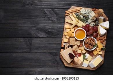 Cheese plate with honey, grapes and nuts on black wooden table, top view. Space for text - Shutterstock ID 1956293113