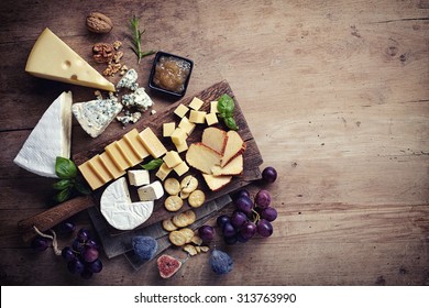 Cheese plate served with grapes, jam, figs, crackers and nuts on a wooden background