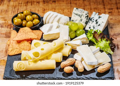 Cheese plate served with grapes, various cheese on a platter.Assorted different types of cheese on a black flat board with olives and nuts. Cheese plate on a wooden table. - Powered by Shutterstock