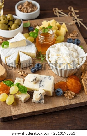 Cheese plate with a variety of cheeses, honey, grapes, nuts, olives, blueberries and fresh herbs on a dark wooden background. A festive snack. Top view, copy space.
