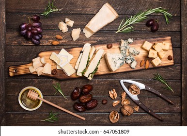 Cheese platter with different cheeses, grapes, nuts, honey, bread and dates on rustic wooden background. Retro styled cheese variety selection on dark wood board. - Powered by Shutterstock