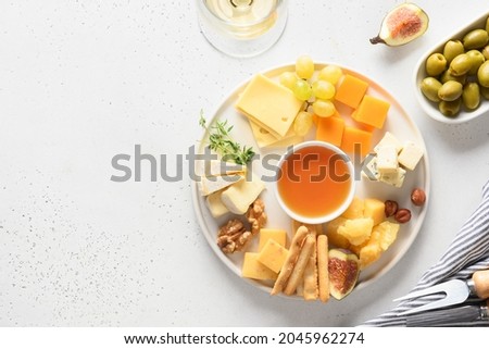 Cheese platter with different cheese and grapes, nuts, olive, figs on a white background with copy space. Top view. Festive gourmet appetizer.