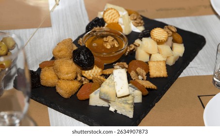 Cheese platter with honey, dried fruits, crackers, and nuts on a black slate background, representing gourmet appetizer concept