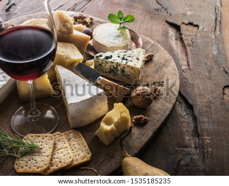 Cheese platter with organic cheeses, fruits, nuts and wine on wooden background. Tasty cheese starter.