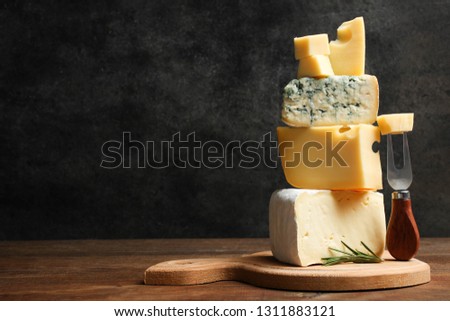 Cheese platter: yellow Maasdam, white Camembert and blue cheese Dor Blue with rosemary and fork on wooden cutting board on black background. Copy space.  Concept serving cheese.