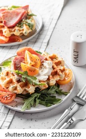 Cheese or potato savory waffles served with with tomatoes, ham and aragula with cutlery. Delisious savory breakfast. Horisontal orientation - Shutterstock ID 2231220109