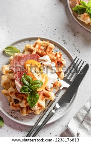 Cheese or potato savory waffles served with yellow tomatoes, cream cheese, ham and bazil leaves with cutlery. Delisious savory breakfast close up. Top view, flat lay
