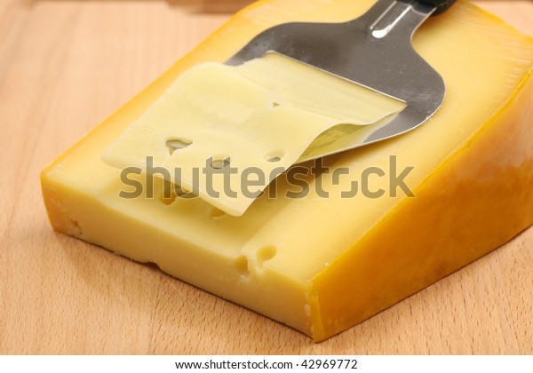 cheese slicer slicing through a block of cheese on\
a wooden cutting board