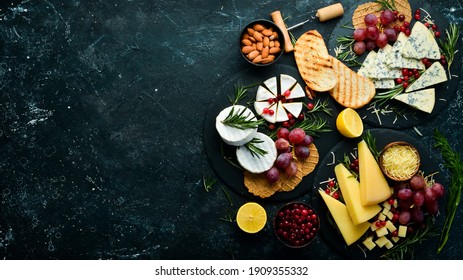 Cheese. Slices of cheese on plates: brie, blue, gorgonzola, parmesan and maasdam on a black stone background. Free copy space. Top view. - Shutterstock ID 1909355332