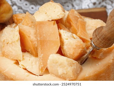 Cheese wheel with slices cut into it and a knife resting inside on a wooden cutting board - Powered by Shutterstock