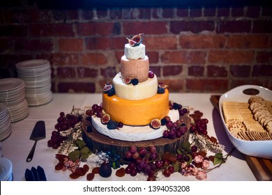 Cheese Wheel Wedding Cake With Rustic Brick Wall Background On Black Walnut Wood Slab Cake Base With Flowers And Dried Fruit