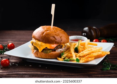 Cheeseburger with beef, tomato, pickles cucumber, red onion, lettuce, cheddar cheese, ketchup and French fries. Tasty burger cooking with beef, tomato, cheese, cucumber and lettuce.