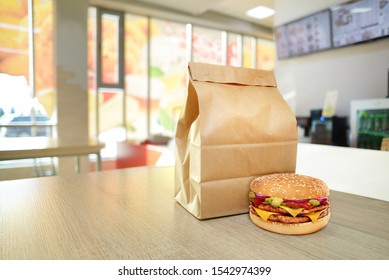 Cheeseburger And Craft Paper Bag On Wooden Counter Of Cafe. Take Out Food Concept. To Go Package Mock-up