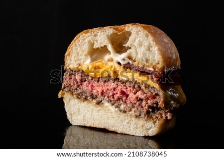 cheeseburger cut in the half showing inside medium rare  beef, melted cheese placed on the top of a reflexive surface and black background.