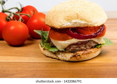 Cheeseburger With Havarti Cheese Tomatoes And Red Onions And Lettuce On A Toasted Cornmeal Bun On A Wooden Table
